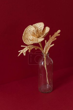 Eine Glasvase mit einem Blumenstrauß aus Stroh auf rotem Hintergrund. Strohflechten