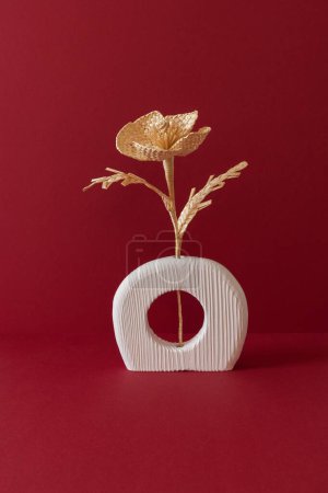Eine hölzerne Vase mit einem Blumenstrauß aus Stroh auf rotem Hintergrund. Strohflechten