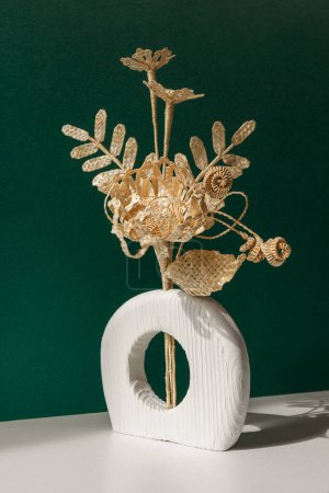A wooden vase with a bouquet of flowers made from straw on a green background. Straw weaving