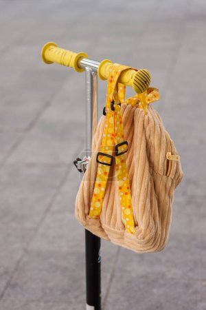 A child's backpack hangs on the handlebars of a scooter