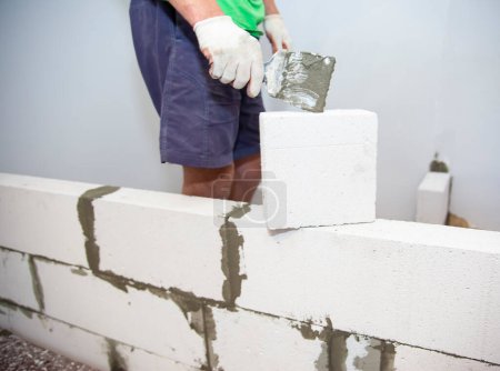 Photo for Plastering the wall.Hand holding a spatula with construction mix.Applying putty or tile glue to with lightweight concrete blocks.Plaster the wall with a putty knife.Internal construction. - Royalty Free Image