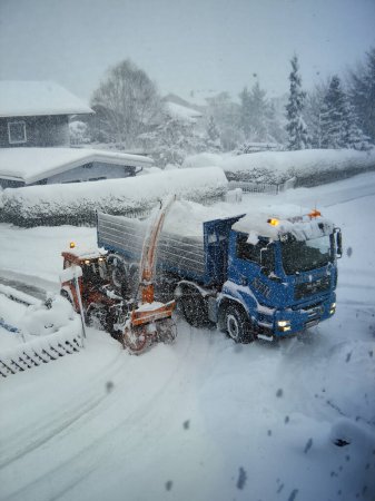 Photo for Blue big truck and snowblower clear snow in mountain city. Snow disaster in the Alps. - Royalty Free Image