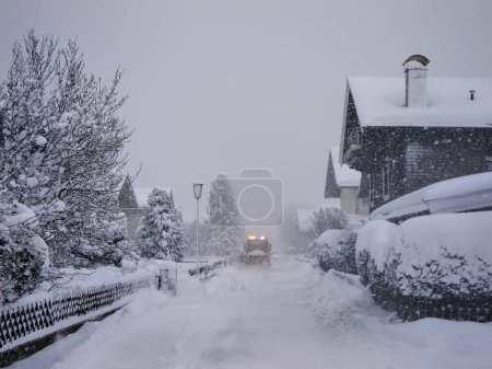 Foto de Mittersill, Austria - La calle está cubierta con una capa alta de nieve y un arado está despejando el camino. Desastre de nieve en los Alpes. - Imagen libre de derechos