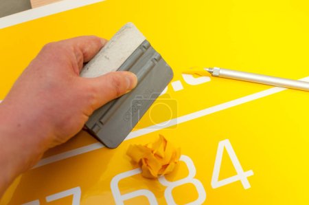 Foto de Close-up of a man's hand making a car sticker from yellow foil - Imagen libre de derechos