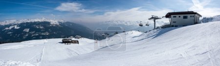 Photo for Upper station of the chairlift in a ski resort in the Austrian mountains. Cable car for skiers and a mountain panorama with a ski slope. - Royalty Free Image