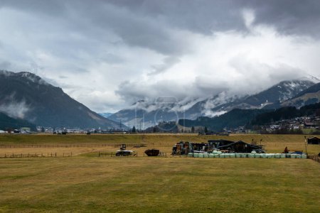 Photo for Valley with mountains in clouds in rainy weather in Austrian Alps. Meadow with outbuildings and hay bales. - Royalty Free Image