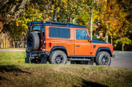 Photo for Brno, Czech Republic - October 15, 2023: Orange Land Rover Defender 90 SUV parked on the road under autumn trees. - Royalty Free Image