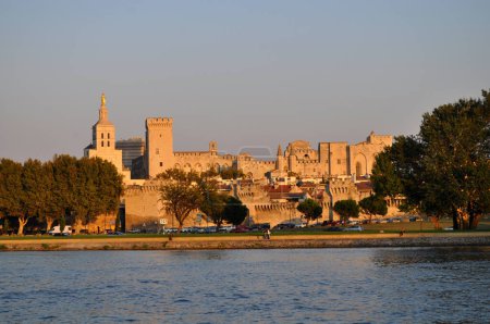 Photo for Papal Palace in the city of Avignon, France illuminated by the setting sun with the river Rhine embankment. - Royalty Free Image