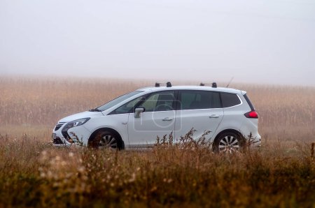 Téléchargez les photos : Voiture MPV famille blanche Opel Zafira se tient sur un terrain dans le brouillard en automne. - en image libre de droit