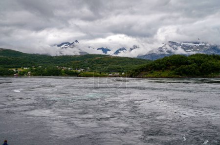 Panorama of snowy mountains in the clouds and water level of the sea in the fjord. Sea eddies on the water - Saltstraumen, Norway