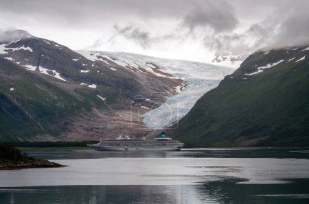 Téléchargez les photos : Un glacier entre montagnes et un grand bateau de croisière flotte à la surface d'un fjord en Norvège. - en image libre de droit