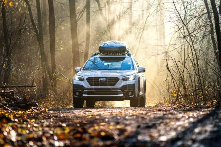 Photo for Brno, Czech Republic - February 15, 2024: White Subaru Outback SUV at sunrise in the forest. The car and the road illuminated by the rays of the sun penetrating through the trees. - Royalty Free Image