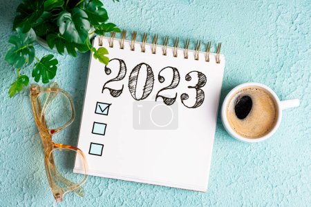 New year goals 2023 on desk. 2023 goals list with notebook, coffee cup, plant on blue table. Resolutions, plan, goals, action, checklist, idea concept. New Year 2023 template, copy space