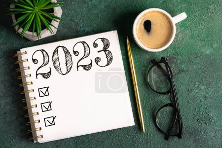 New year resolutions 2023 on desk. 2023 resolutions list with notebook, coffee cup on table. Goals, resolutions, plan, action, checklist concept. New Year 2023 background. Copy spac