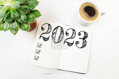 New year resolutions 2023 on white desk. 2023 resolutions list with notebook, coffee cup on table. Goals, resolutions, plan, action, checklist concept. New Year 2023 template, copy spac