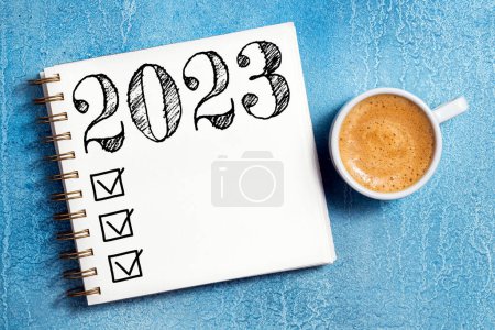 Foto de Resoluciones de año nuevo 2023 en el escritorio. Lista de resoluciones 2023 con cuaderno, taza de café en la mesa. Objetivos, resoluciones, plan, acción, concepto de lista de verificación. Plantilla de año nuevo 2023, copia spac - Imagen libre de derechos