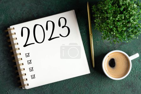 Foto de Resoluciones de año nuevo 2023 en el escritorio. Lista de resoluciones 2023 con cuaderno, taza de café sobre mesa verde. Objetivos, resoluciones, planear, hacer lista, acción, concepto de lista de verificación. Plantilla de año nuevo 2023, copia spac - Imagen libre de derechos