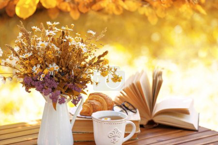 Photo for Bouquet of flowers, croissant, cup of tea or coffee, books on table in autumn garden. Rest in garden, reading books, breakfast, vacations in nature concept. Autumn time in garden on backyard - Royalty Free Image
