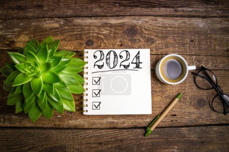 Neujahrsvorsätze 2024 auf dem Schreibtisch. 2024-Tore-Liste mit Notizbuch, Kaffeetasse, Pflanze auf Holztisch. Vorsätze, Pläne, Ziele, Maßnahmen, Checkliste, Ideenkonzept. Neujahrsvorsätze 2024, Kopierraum