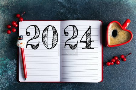 Neujahrsvorsätze 2024 auf dem Schreibtisch. 2024-Tore-Liste mit Notizbuch, Kaffeetasse auf blauem Tisch. Vorsätze, Pläne, Ziele, Maßnahmen, Checkliste, Ideenkonzept. Neujahrsvorsätze 2024, Kopierraum