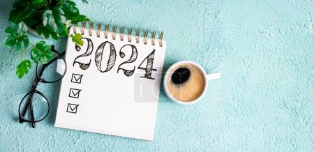 Nouvelles résolutions de l'année 2024 sur le bureau. Liste des résolutions 2024 avec cahier, tasse à café sur la table. Buts, résolutions, plan, action, concept de liste de contrôle. Nouvel An 2024 modèle, espace de copie