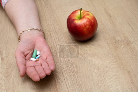 Foto de A woman's hand with medicines next to an apple lying on the table - Imagen libre de derechos