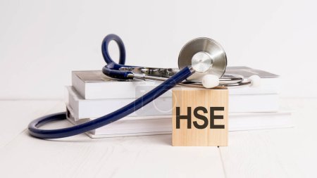 text HSE is written on wooden cube near a stethoscope on a white background