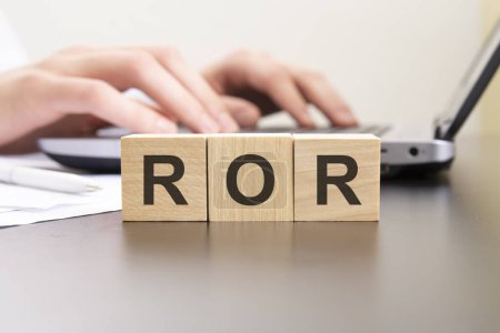 ROR - Abkürzung aus Holzblöcken mit Buchstaben. Hintergrund Hände auf einem Laptop mit Unschärfe