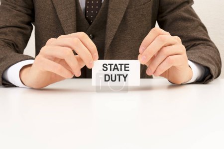 state duty is written on a white business card in a man's hand. Brown background. Business and advertising concept