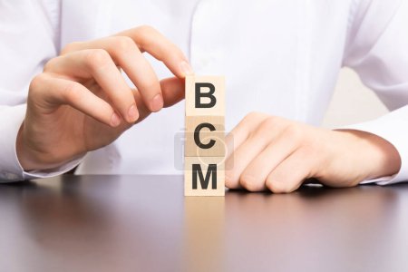 bcm, business continuity management text on cube blocks in businessman hands, white background