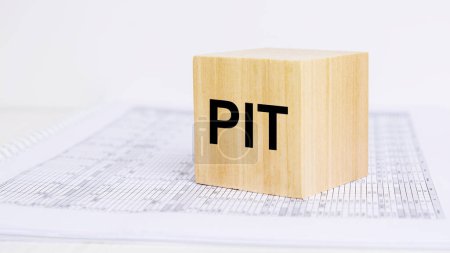 Téléchargez les photos : Un grand bloc de bois avec les lettres PIT se trouve sur une feuille de calcul. concept d'impôt sur le revenu des particuliers - en image libre de droit
