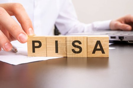 PISA-Wort aus Holzklötzen auf dem Laptop im Hintergrund. Selektiver Fokus.