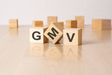 GMV - an abbreviation of wooden blocks with letters on a gray background. reflection caption on the mirrored surface of the table.