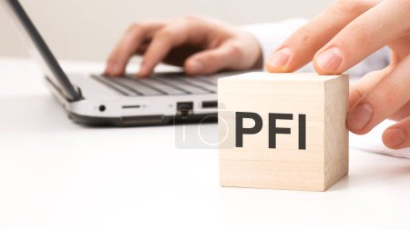 Photo for Man holding wooden cube witt letters PFI in the background a laptop on a white office table background - Royalty Free Image