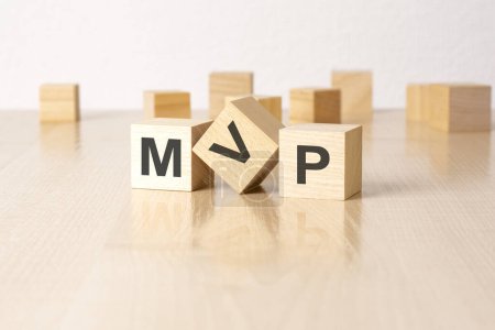 mvp - an abbreviation of wooden blocks with letters on a gray background. reflection caption on the mirrored surface of the table.