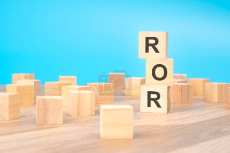 ROR - short for Rate Of Return - written on a wooden cube, business concept. blue background
