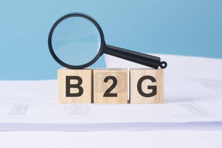 B2G word on wooden cubes on a blue background with magnifier and business documents.