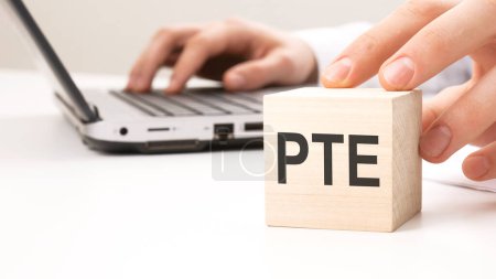 Mann hält hölzernen Würfel Witze Buchstaben PTE im Hintergrund einen Laptop auf einem weißen Bürotisch Hintergrund
