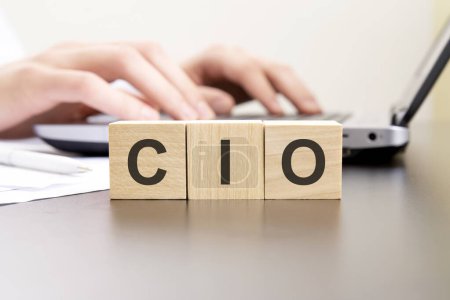 CIO - acronym from wooden blocks with letters. background hands on a laptop with blur