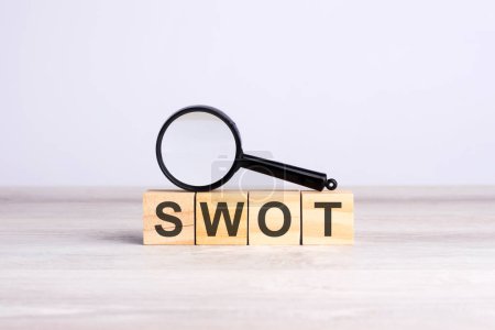 magnifying glass and wooden blocks with the text: SWOT. can be used for business, marketing and education concept