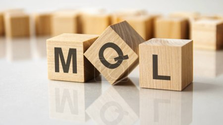 MQL - eine Abkürzung für Holzklötze mit Buchstaben auf grauem Hintergrund. Spiegelung der MQL-Beschriftung auf der gespiegelten Oberfläche der Tabelle. Selektiver Fokus.