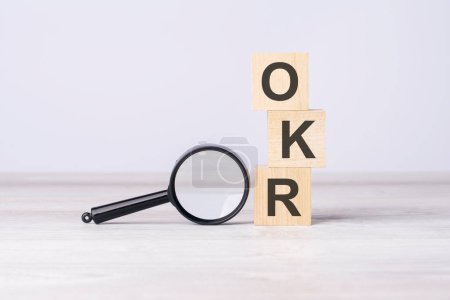 OKR - or Objectives and Key Results concept. text on wooden cubes under a magnifying glass.