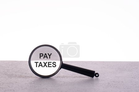 PAY TAXES text through a magnifying glass written on a light background.