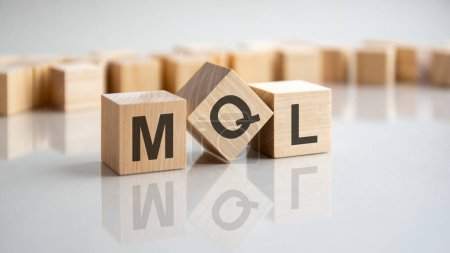 MQL - eine Abkürzung für Holzklötze mit Buchstaben auf grauem Hintergrund. Spiegelung der MQL-Beschriftung auf der gespiegelten Oberfläche der Tabelle. Selektiver Fokus.