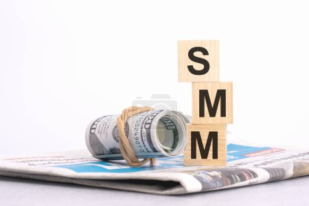 Holzwürfelblock mit dem Text der SMM auf dem Hintergrund einer Zeitung und Banknoten. Finanz-, Management-, Wirtschafts-, Geschäftskonzept