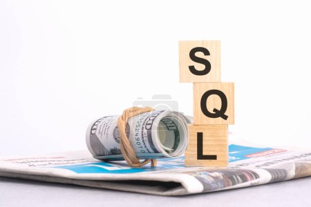 Holzwürfelblock mit dem Text von SQL auf dem Hintergrund einer Zeitung und Banknoten. Finanz-, Management-, Wirtschafts-, Geschäftskonzept