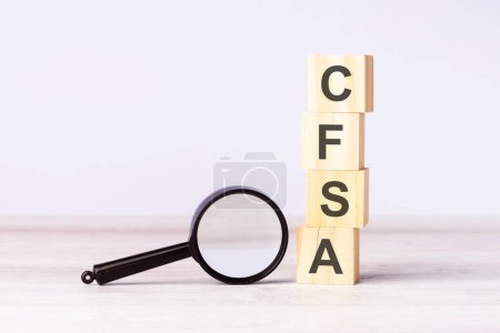 Linse und Holzwürfel mit Text CFSA auf Holztisch, grauer Hintergrund