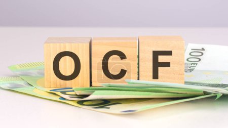 ocf - texto sobre cubos de madera con billetes de euro. vista frontal