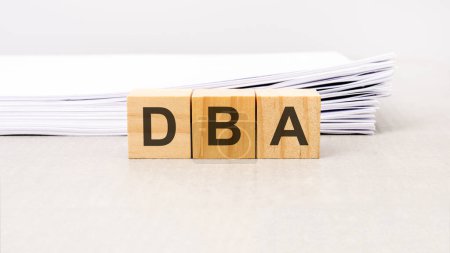 Text DBA - Datenbank-Administrator aus Holzbausteinen, Stapelweißes Papier auf Hintergrund