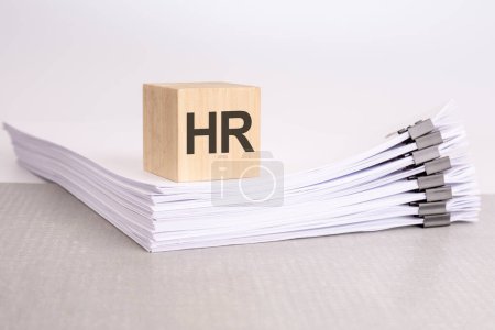 a wooden block with a text HR on a stack of documents. grey table, white background